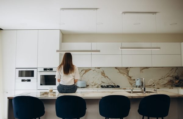 Young beautiful brunette in casual clothes sits in kitchen with fresh drink at morning time. young woman sitting at the kitchen table with her back to the camera. rear view